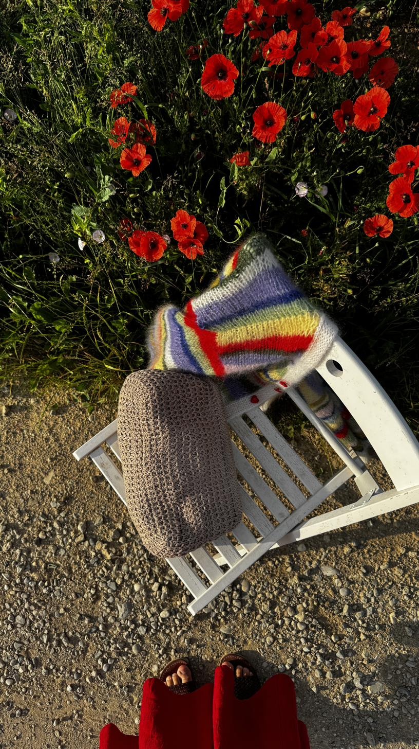 Striped mohair cardigan draped over a chair beside a bed of red poppies